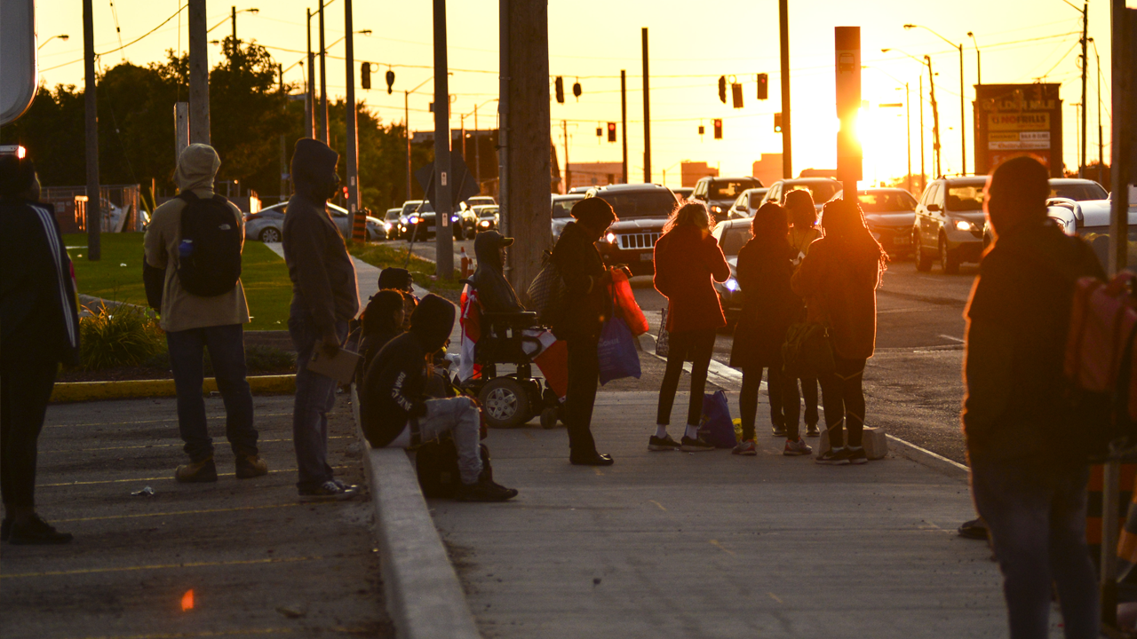 Residents of Scarborough’s Greater Golden Mile wait at a bus stop at sunset.