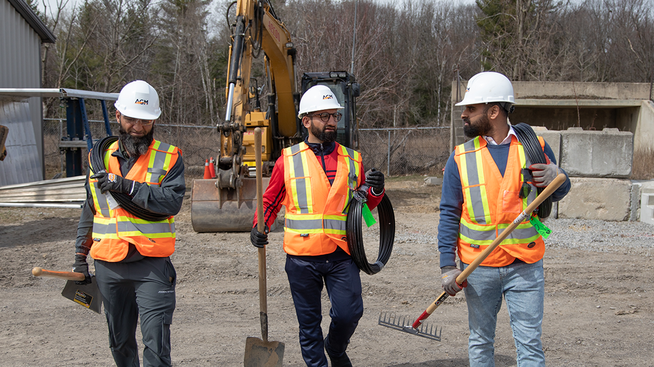 Three ILEO construction workers walk carrying shovels and rakes.