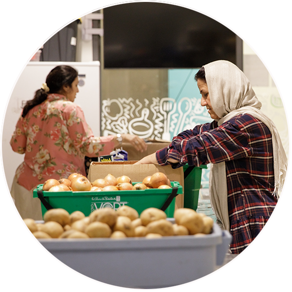Two women pack boxes of food, with potatoes and onions in the foreground