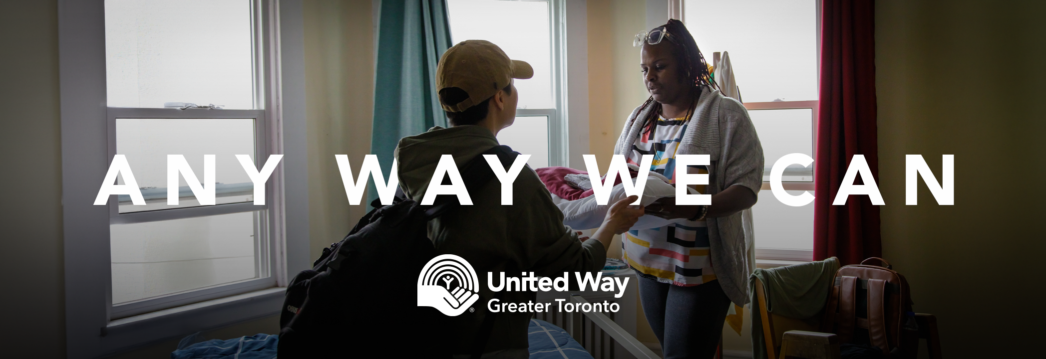 A person wearing a cap receives a pillow from a Black woman, with the words ‘Any way we can’ and the United Way Greater Toronto logo in white.