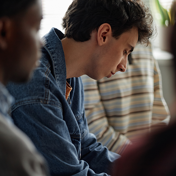 Close-up of a young man in a denim jacket looking down thoughtfully.
