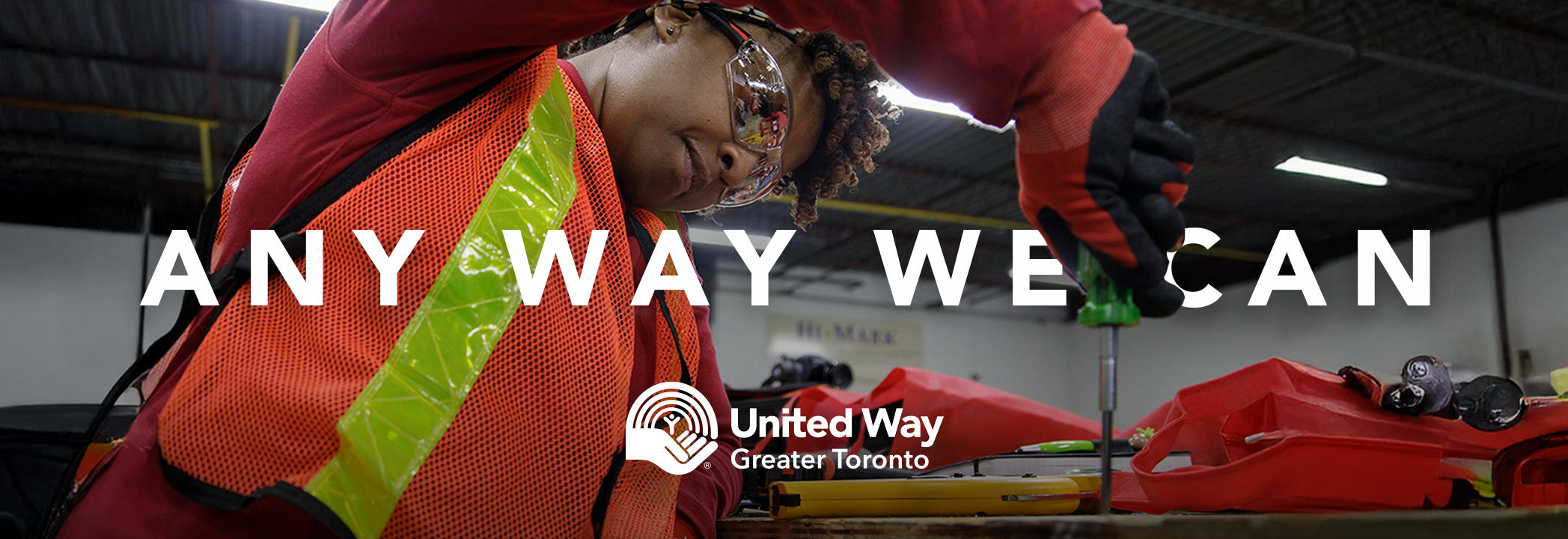 Person wearing a safety vest and goggles tightens a screw with white text reading “Any way we can” and the United Way Greater Toronto Logo below the text