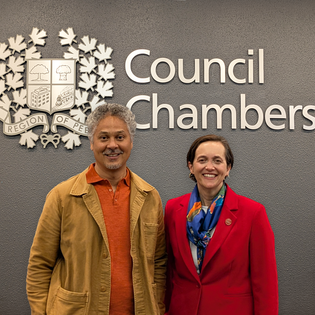 United Way’s Vice President of Community Impact and Mobilization Nation Cheong and United Way President & CEO Heather McDonald stand next to one another, smiling in front of the Peel Regional Council Chambers sign.