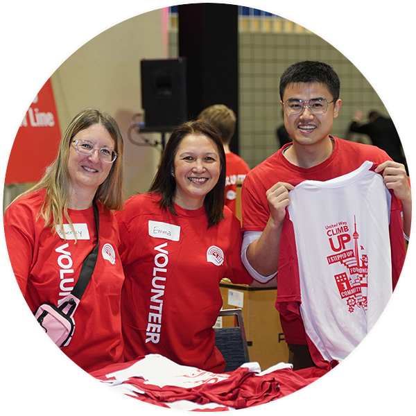 Circle shaped photo of three people wearing volunteer shirts at ClimbUP behind a table of shirts.
