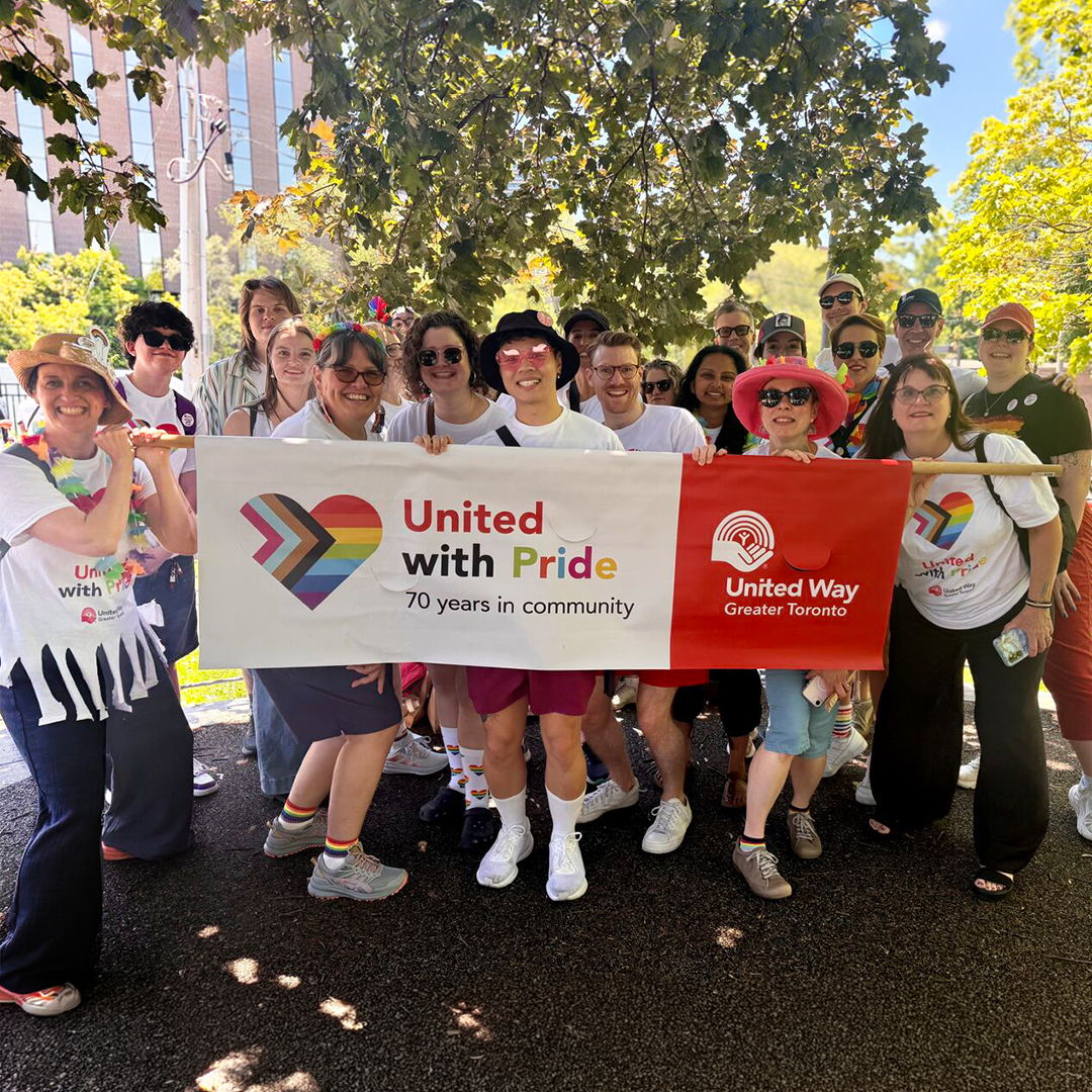 United Way staff at the Pride Parade pose with a branded sign that says “United With Pride” and “70 years in community”