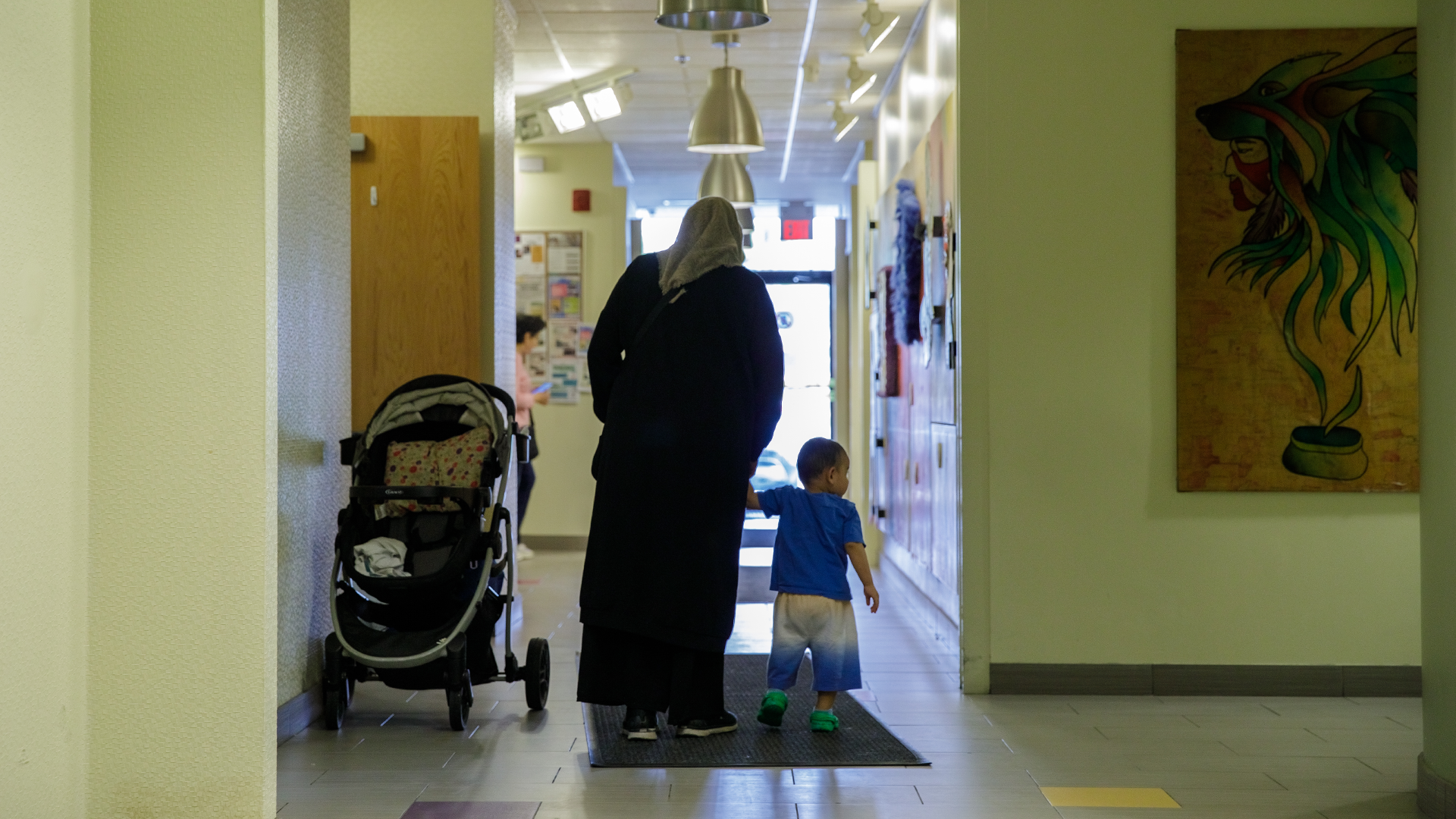 A woman and young child face away from the camera, walking down a hallway inside Dorset Park Community Hub.