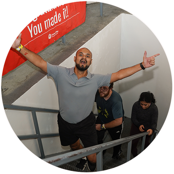 A ClimbUP participant climbs the CN Tower stairwell with arms outstretched beneath a red “You made it!” banner, while other participants continue climbing behind.