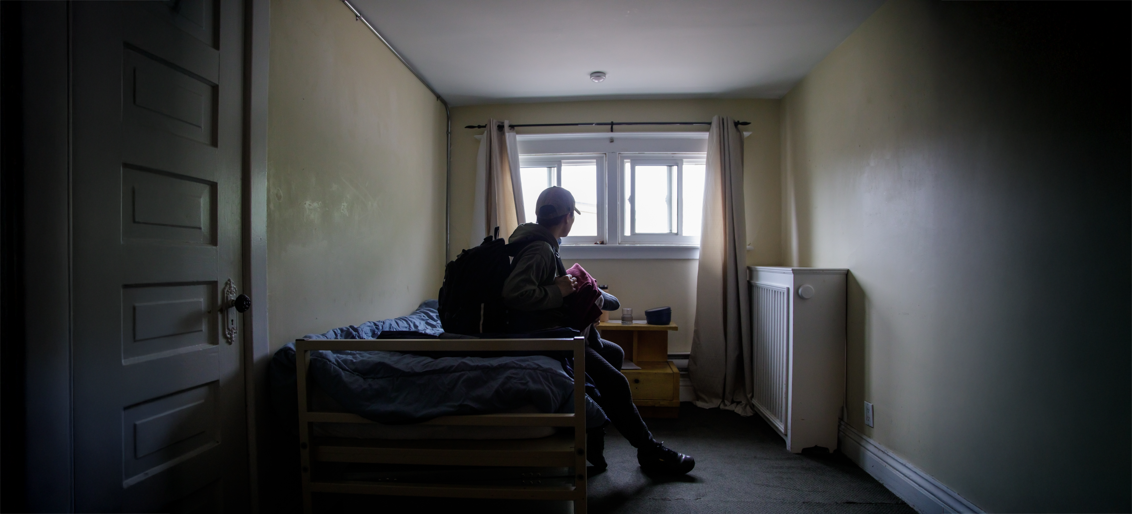 Youth sitting in homeless shelter with backpack and belongings